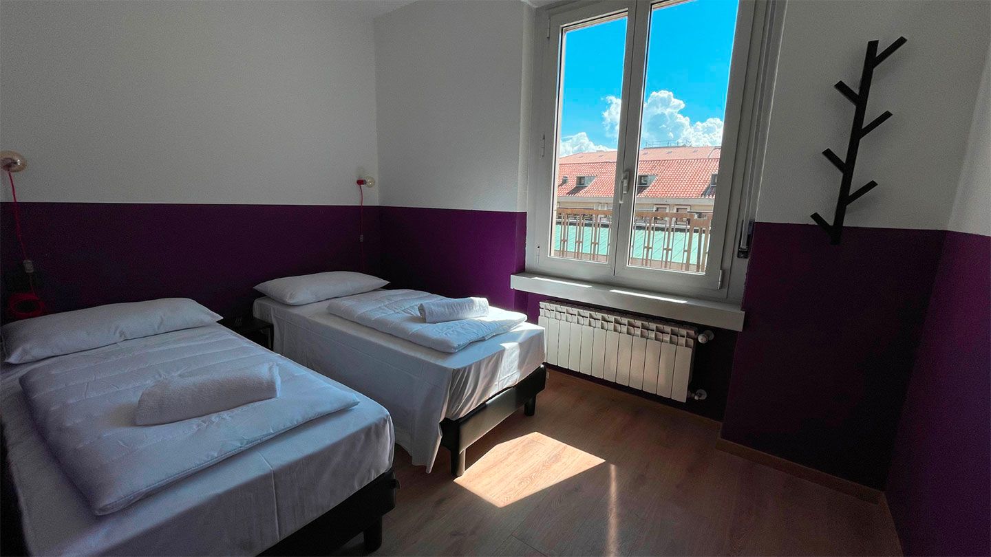 Due letti singoli in una stanza con parete viola, finestra con vista e attaccapanni.