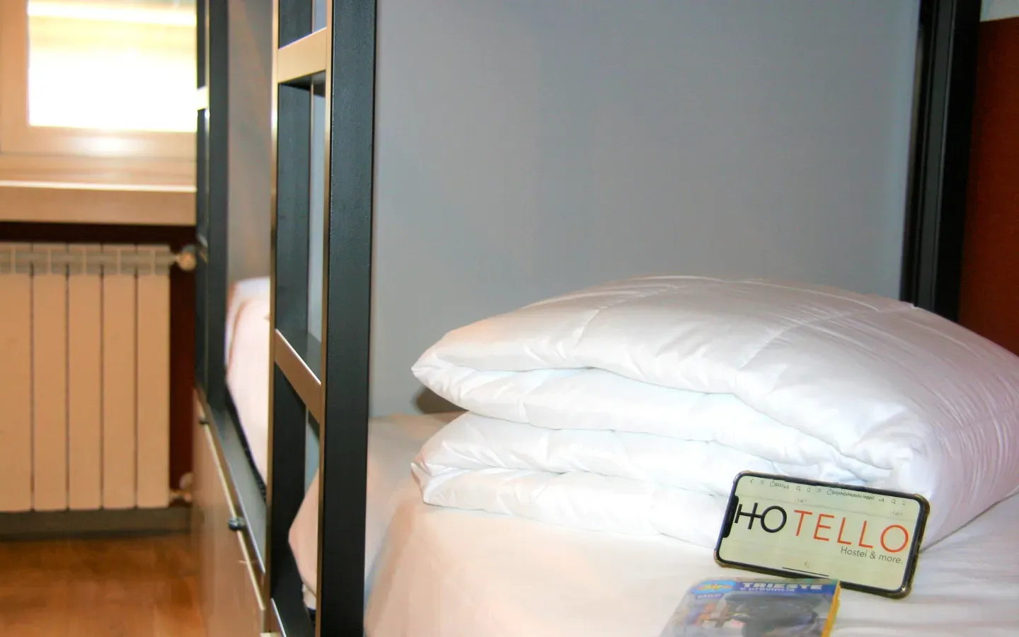 Letto a castello con lenzuola bianche, finestra, termosifone e cartello 