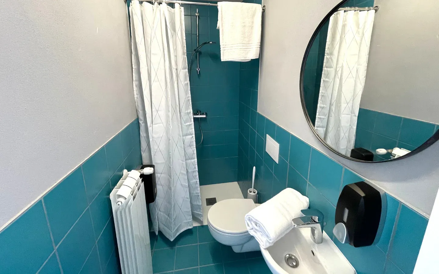 Piccolo bagno turchese con WC, bidet, doccia, specchio e asciugamano.