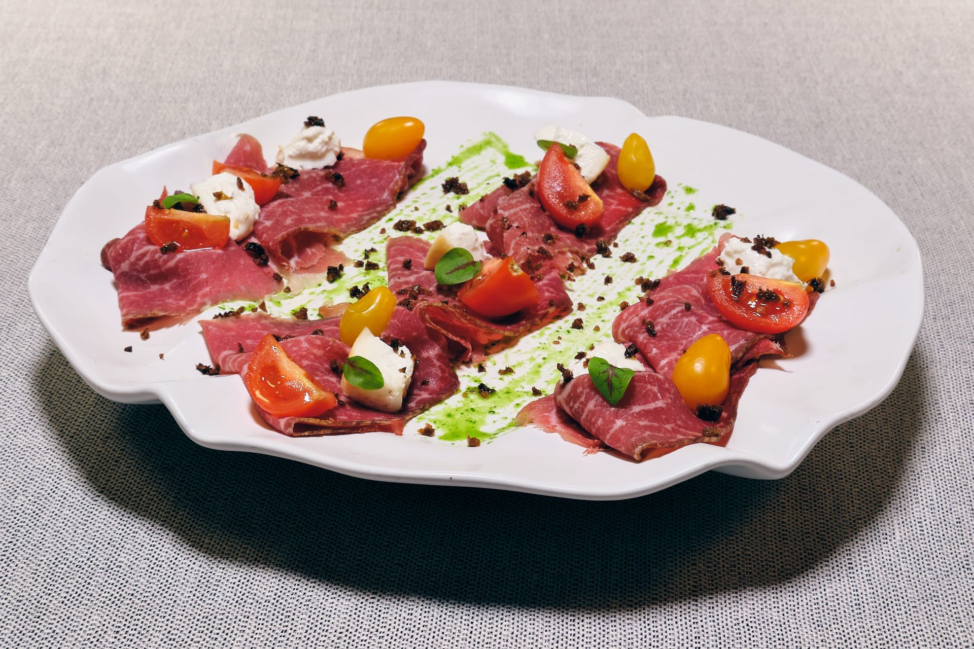 Antipasto di carpaccio su piatto bianco con pomodori, mozzarella ed erbe aromatiche.