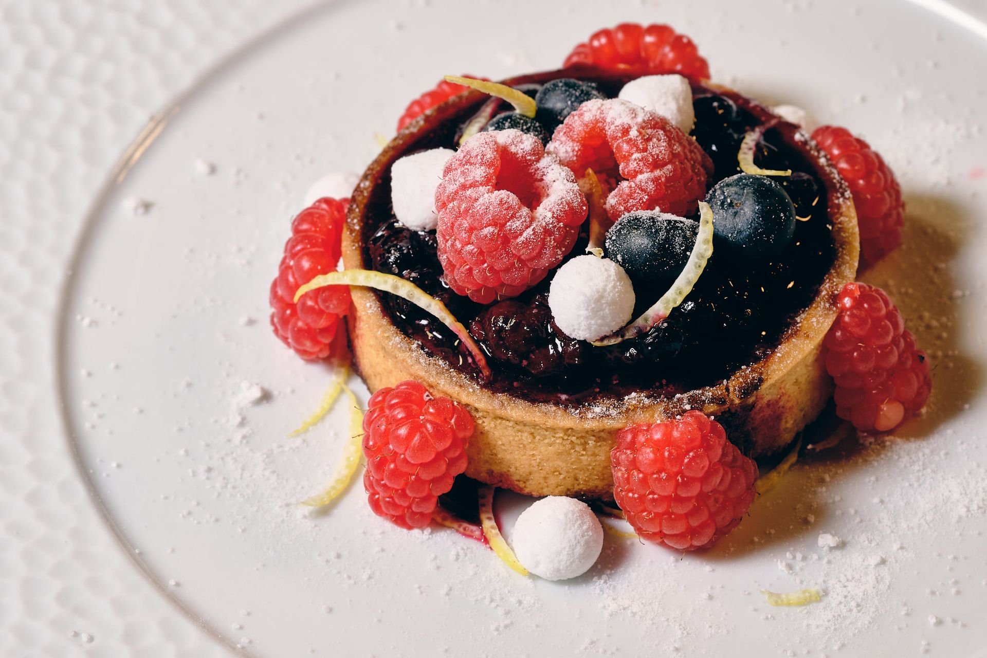 Crostata di frutti di bosco su un piatto bianco, con lamponi, mirtilli e zucchero a velo.