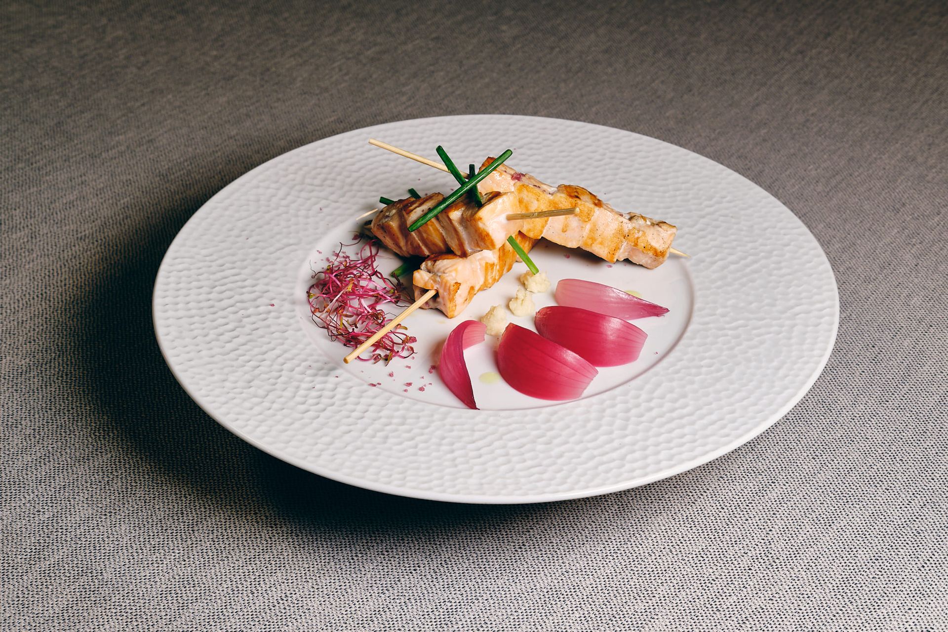 Spiedini di salmone su un piatto bianco con purea di barbabietola e fette di cipolla rossa.