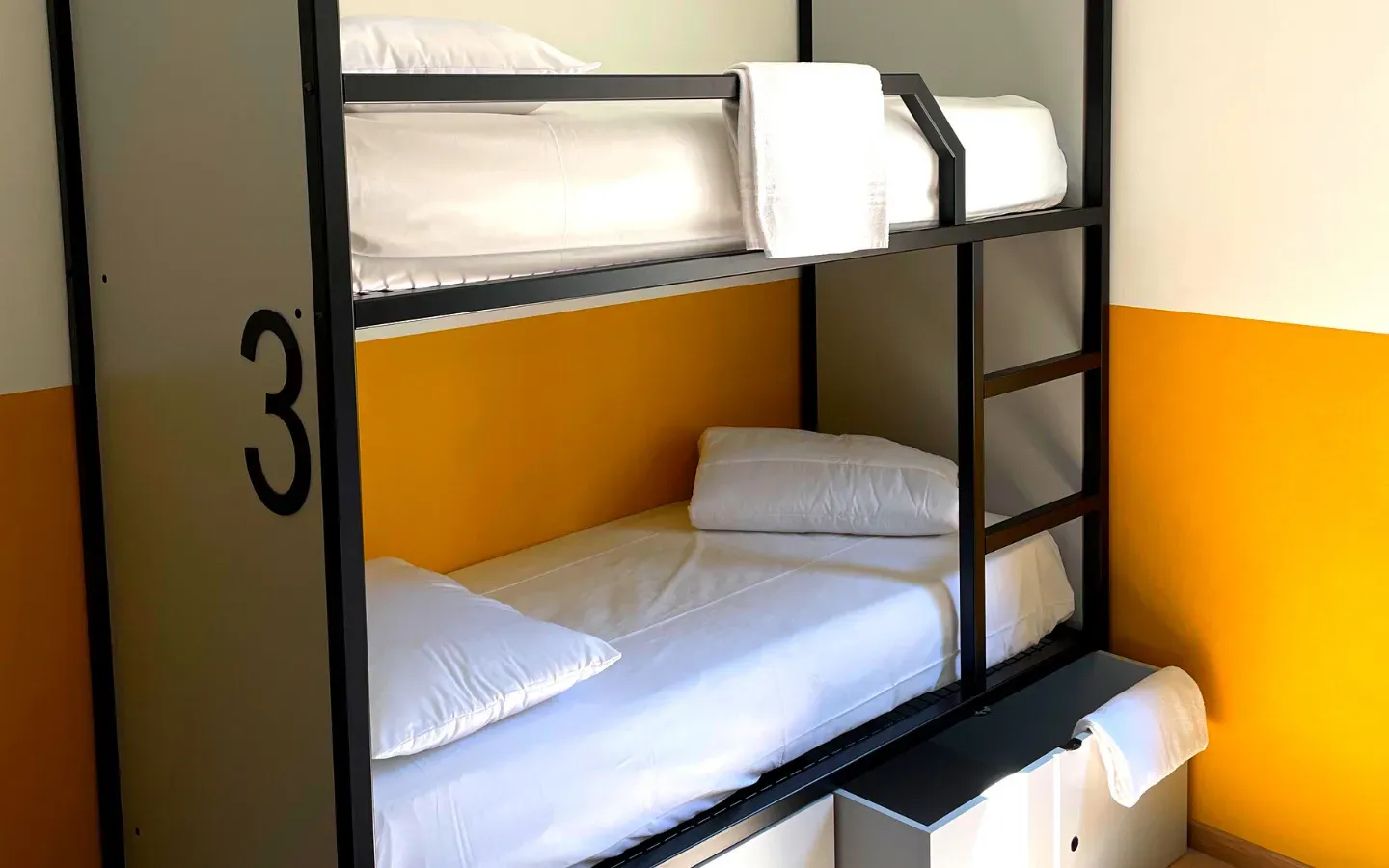 Letti a castello con lenzuola bianche in una stanza con pareti arancioni e bianche. Il numero 3 è sul lato.