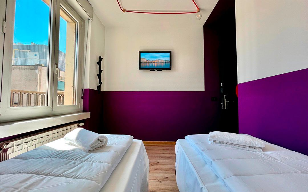 Due letti in una camera d'albergo con parete decorata in viola, finestra e TV.