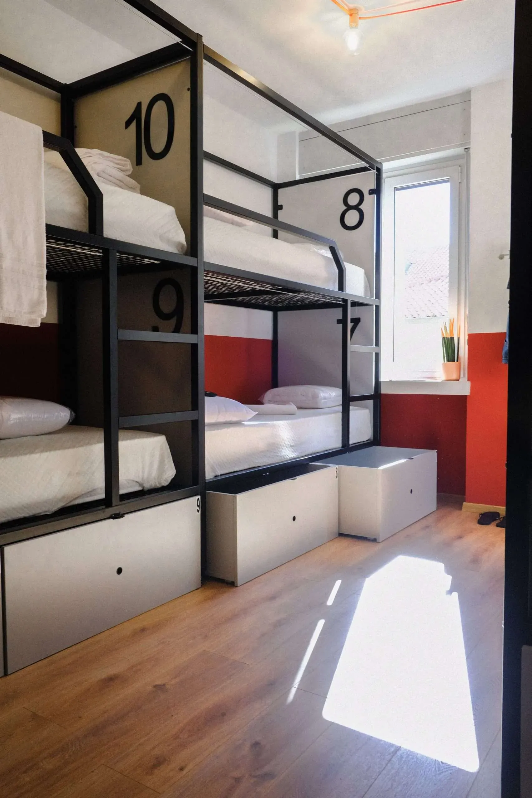 Letti a castello in una stanza con pavimenti in legno, pareti rosse e una finestra; letti etichettati 7, 8, 9 e 10.