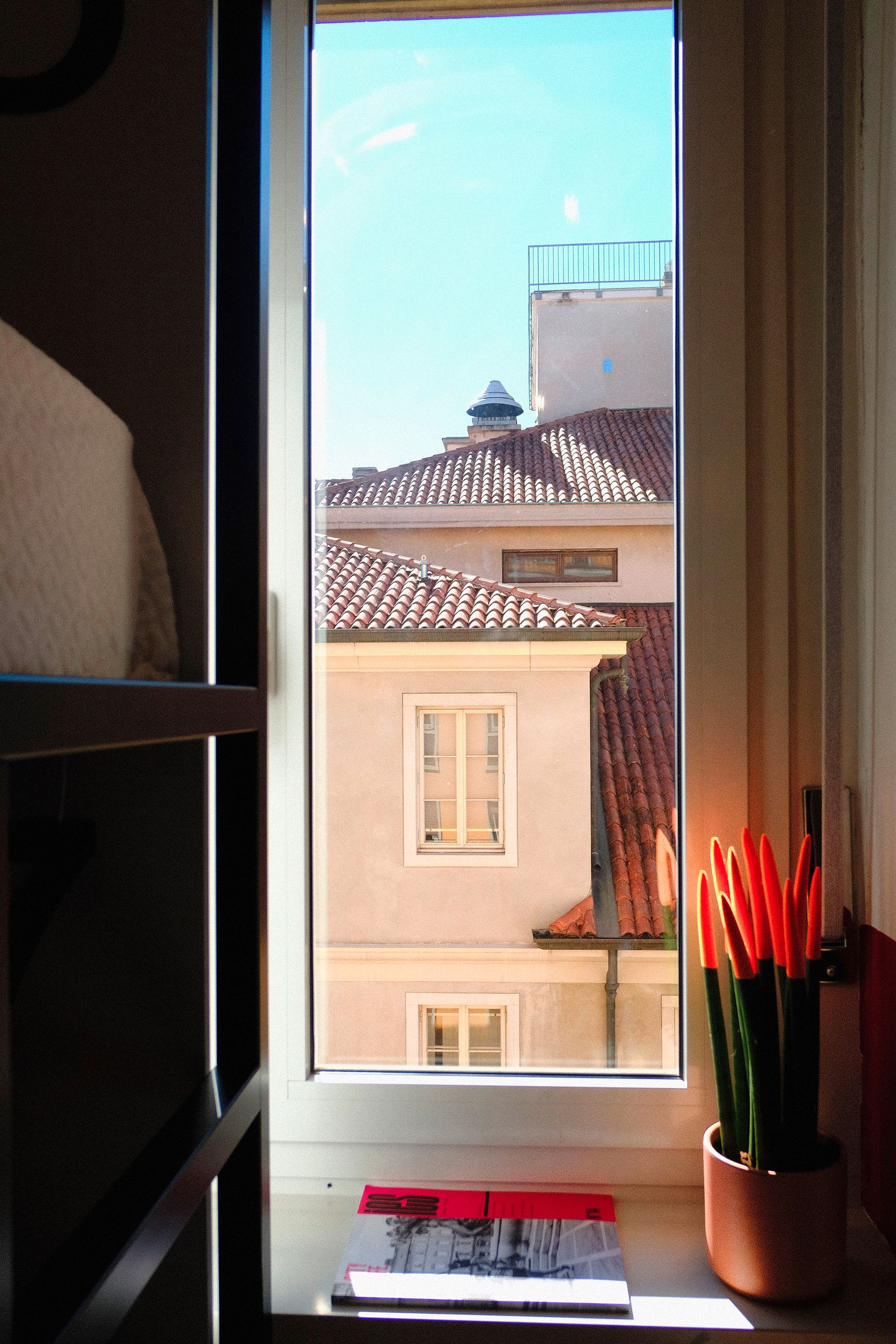 Vista dalla finestra di edifici con tetti di tegole rosse e un cielo azzurro brillante.