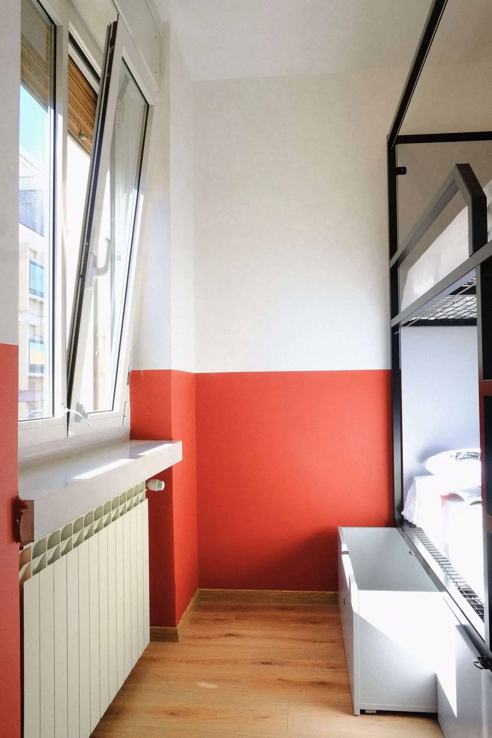 Stanza stretta con letto a castello, finestra. Pareti dipinte di rosso e bianco.