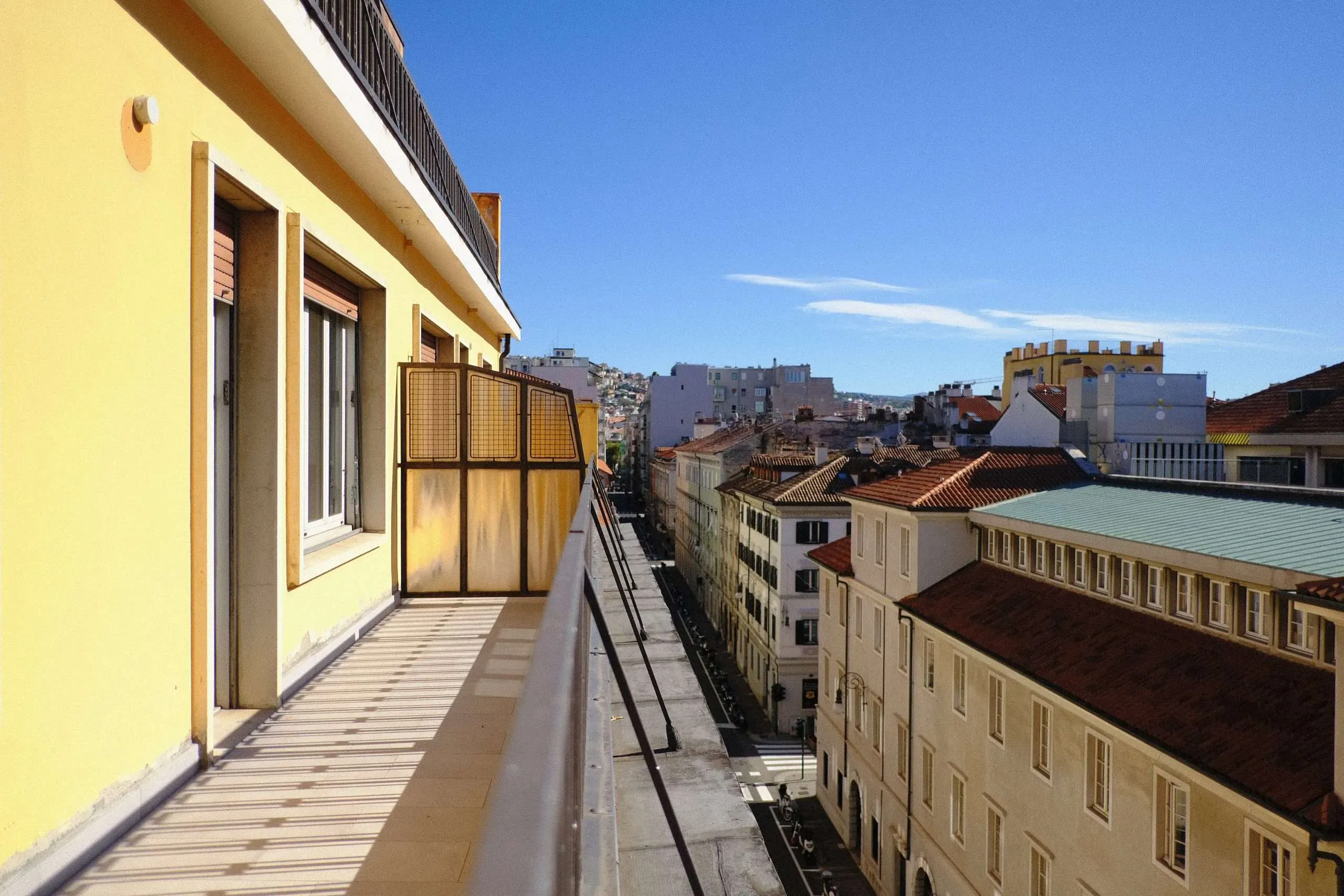 Balcone con vista su una strada cittadina con edifici, giornata di sole e cielo azzurro.