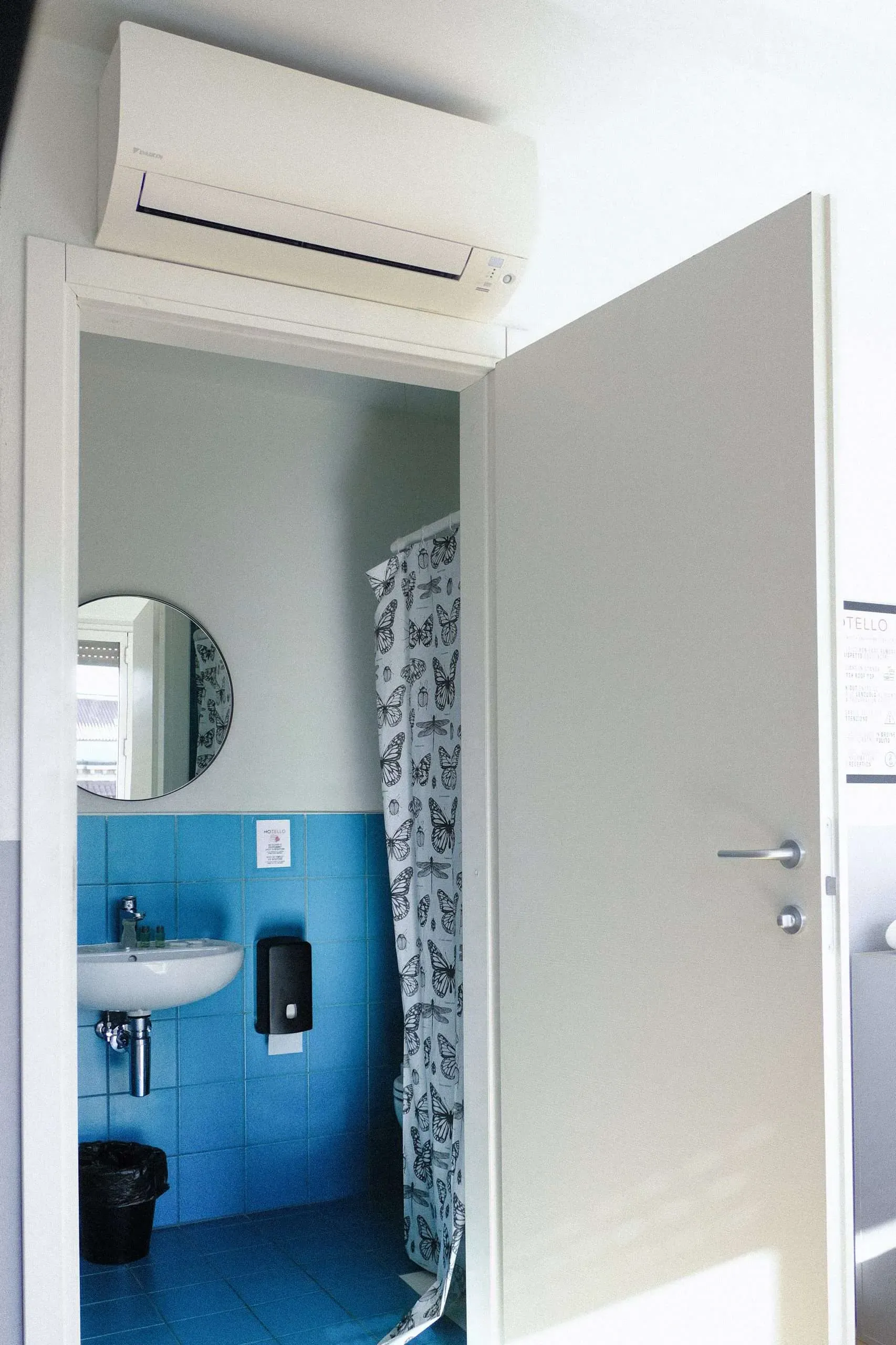 Una porta bianca aperta rivela un piccolo bagno con una parete piastrellata blu.