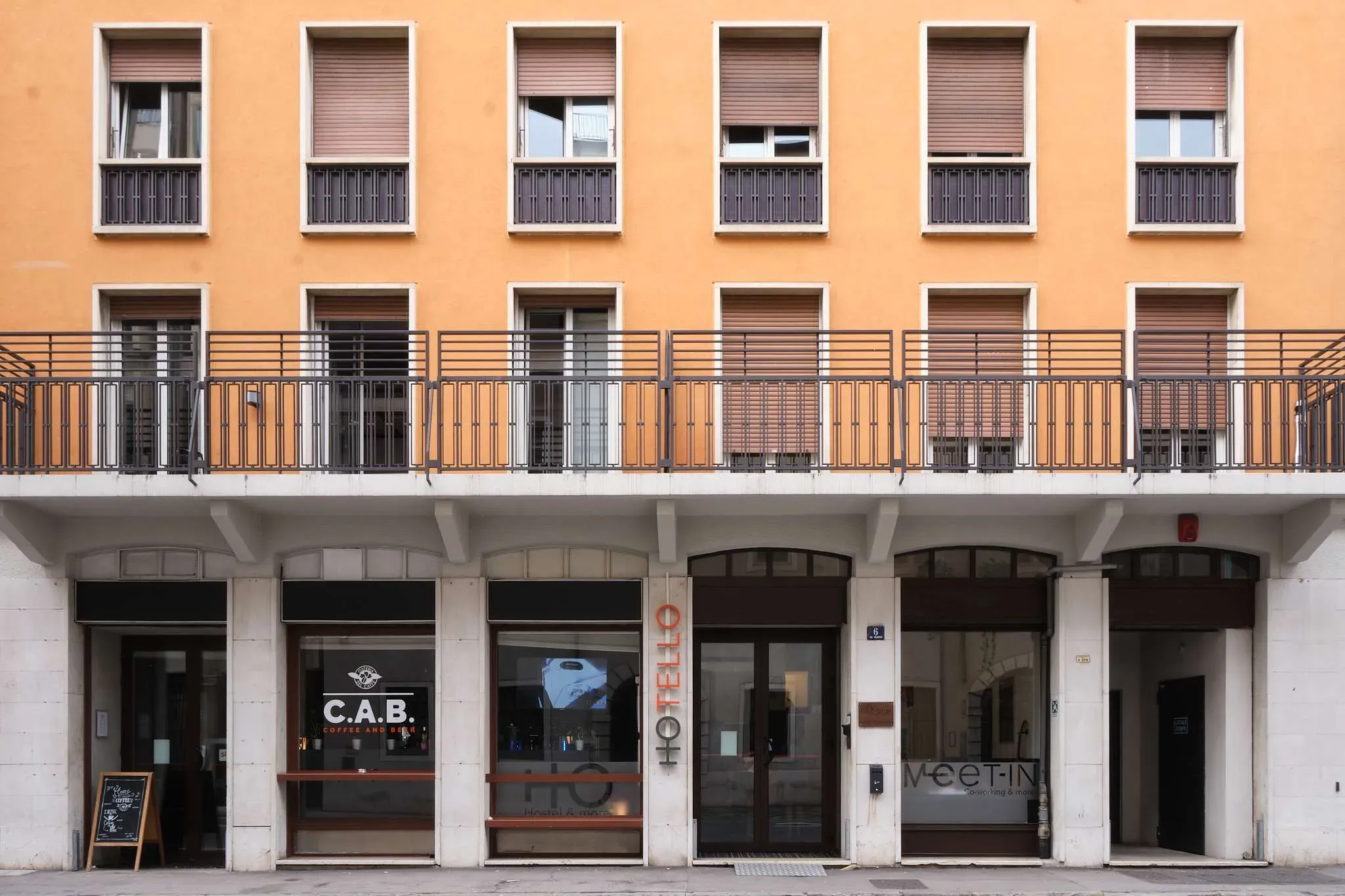 Facciata dell'edificio con pareti arancioni, file di finestre e attività commerciali al piano terra.