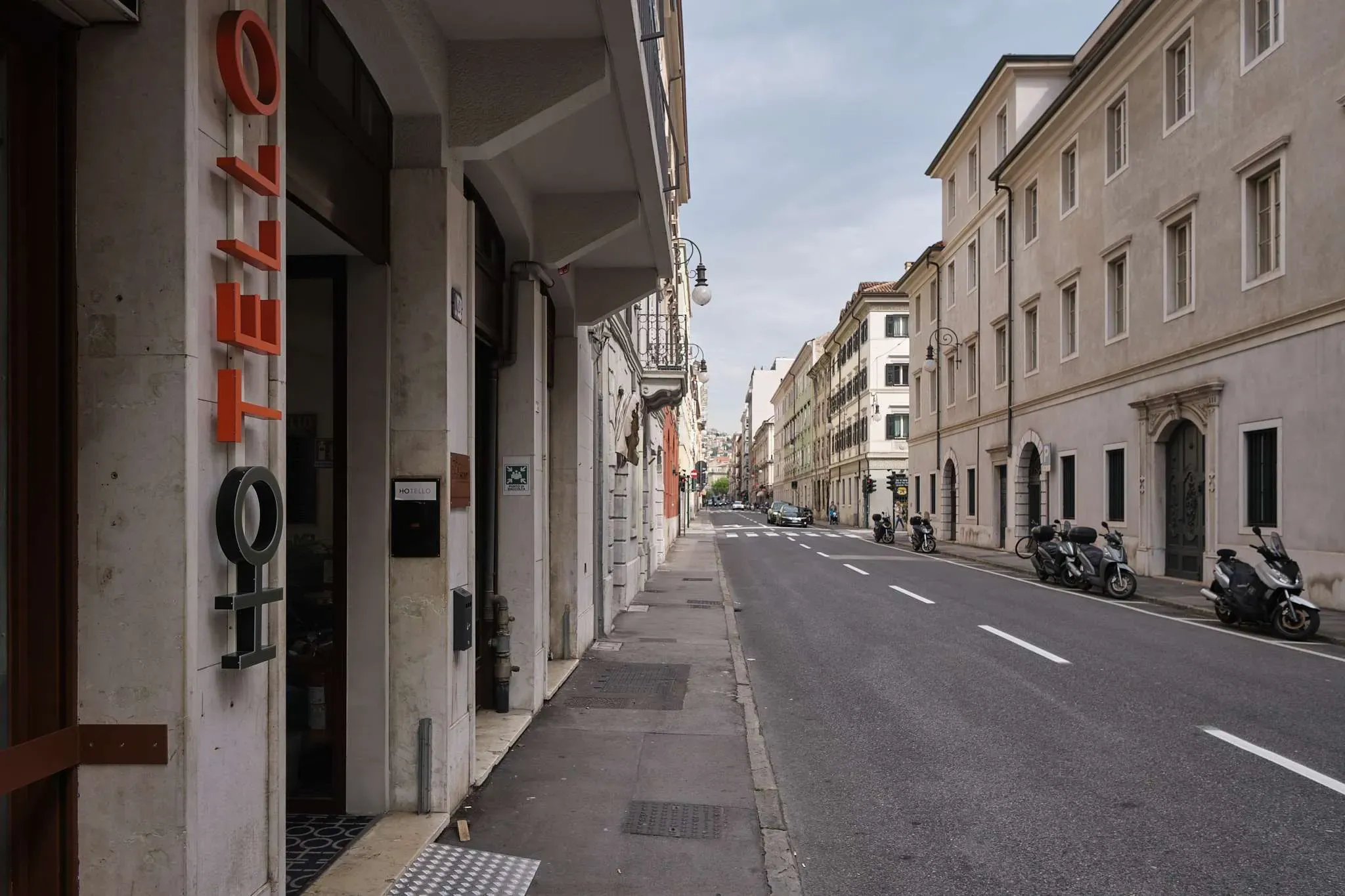 Veduta stradale con edifici, un marciapiede e una strada. È visibile l'insegna di un hotel.