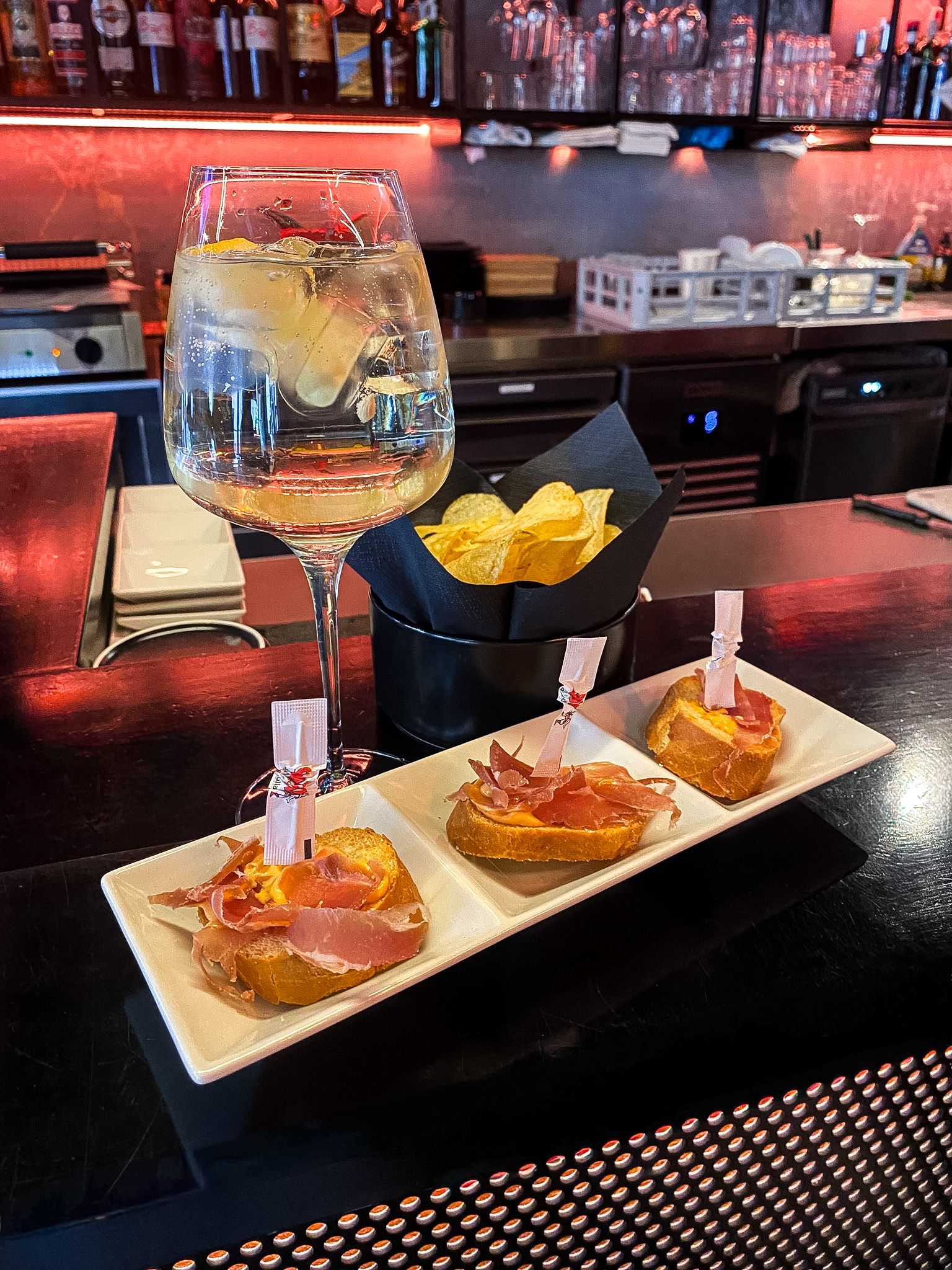 Persona che regge un vassoio con bevande al bar: vino rosso in un bicchiere, cocktail e caffè con schiuma.