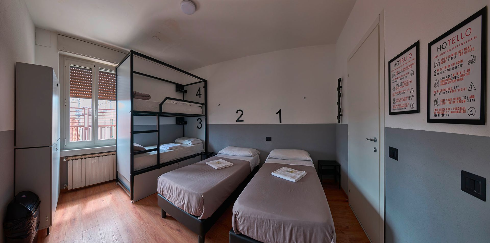 Una stanza in ostello con due letti singoli e un letto a castello. Le pareti sono grigie e bianche.