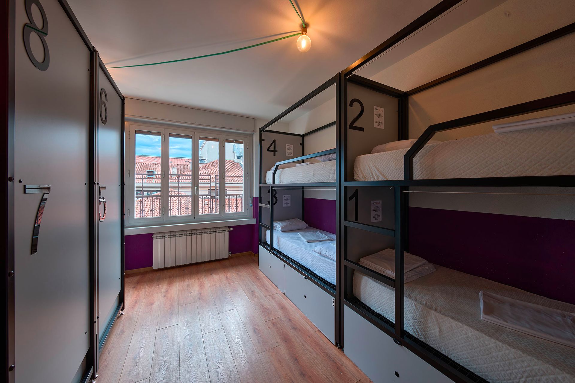 Camerata in ostello con letti a castello, armadietti e finestra con vista sulla città.
