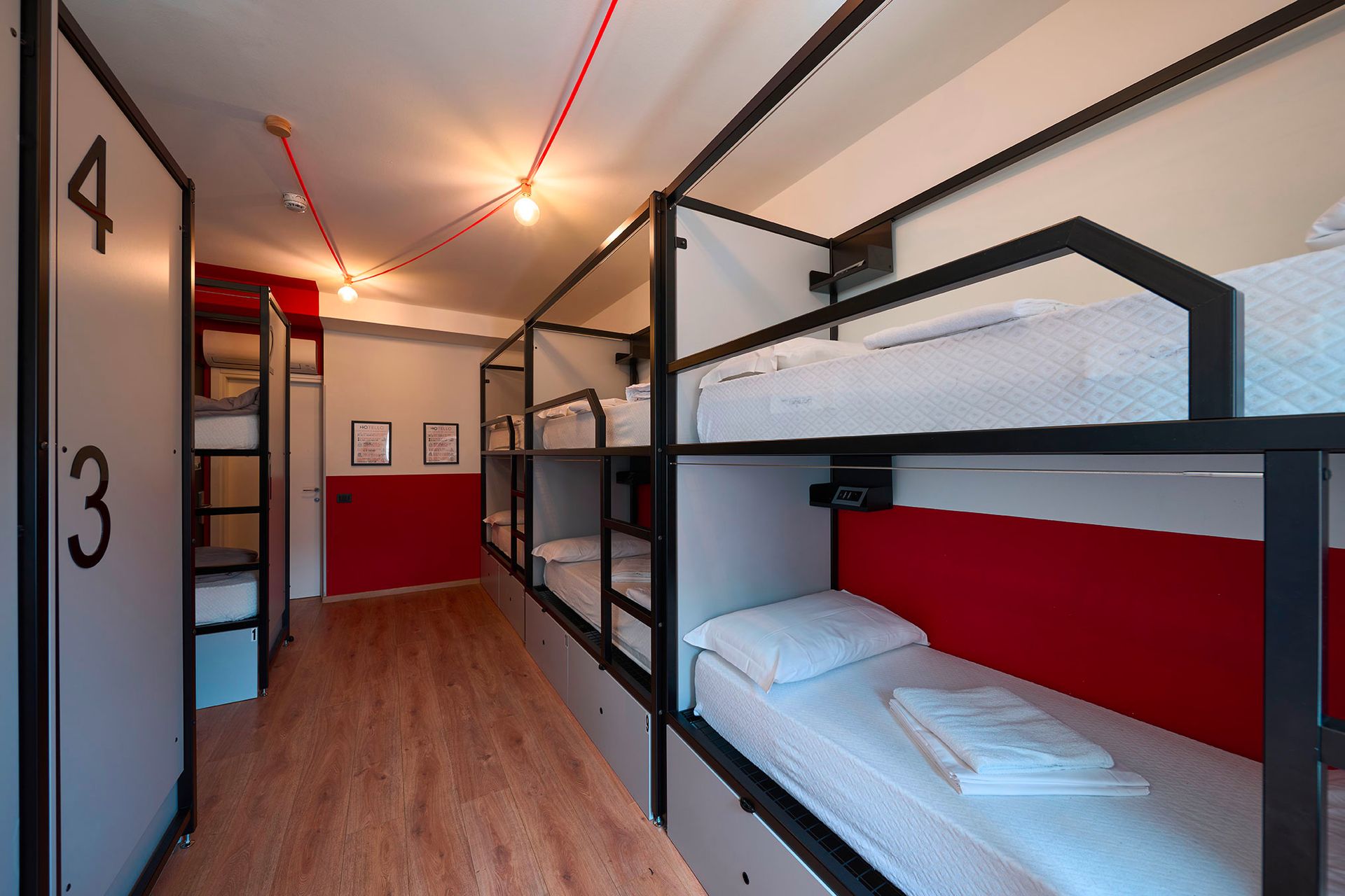 Dormitorio dell'ostello con più letti a castello, dettagli rossi e pavimento in legno.