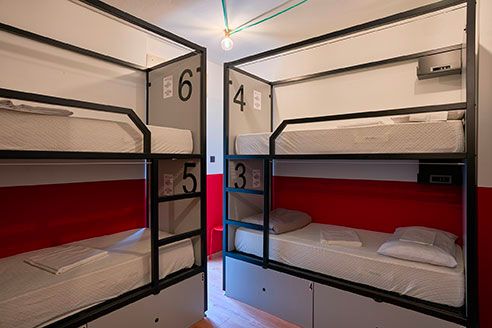 Letti a castello in una stanza di un ostello: due set con pareti rosse e grigie, etichettati 3-6.