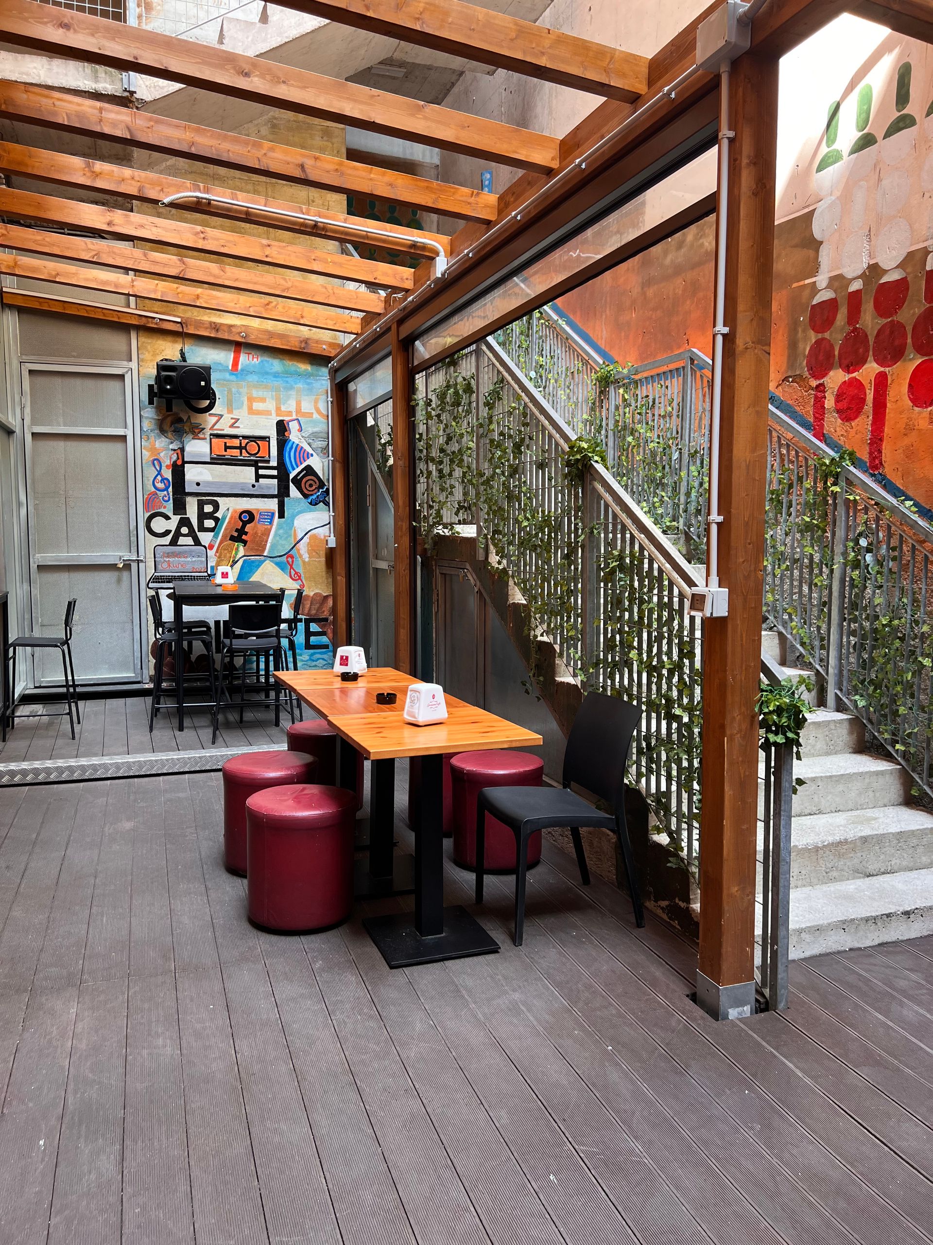 Area salotto all'aperto con tavolo e sgabelli; scala con piante; murale sulla parete.