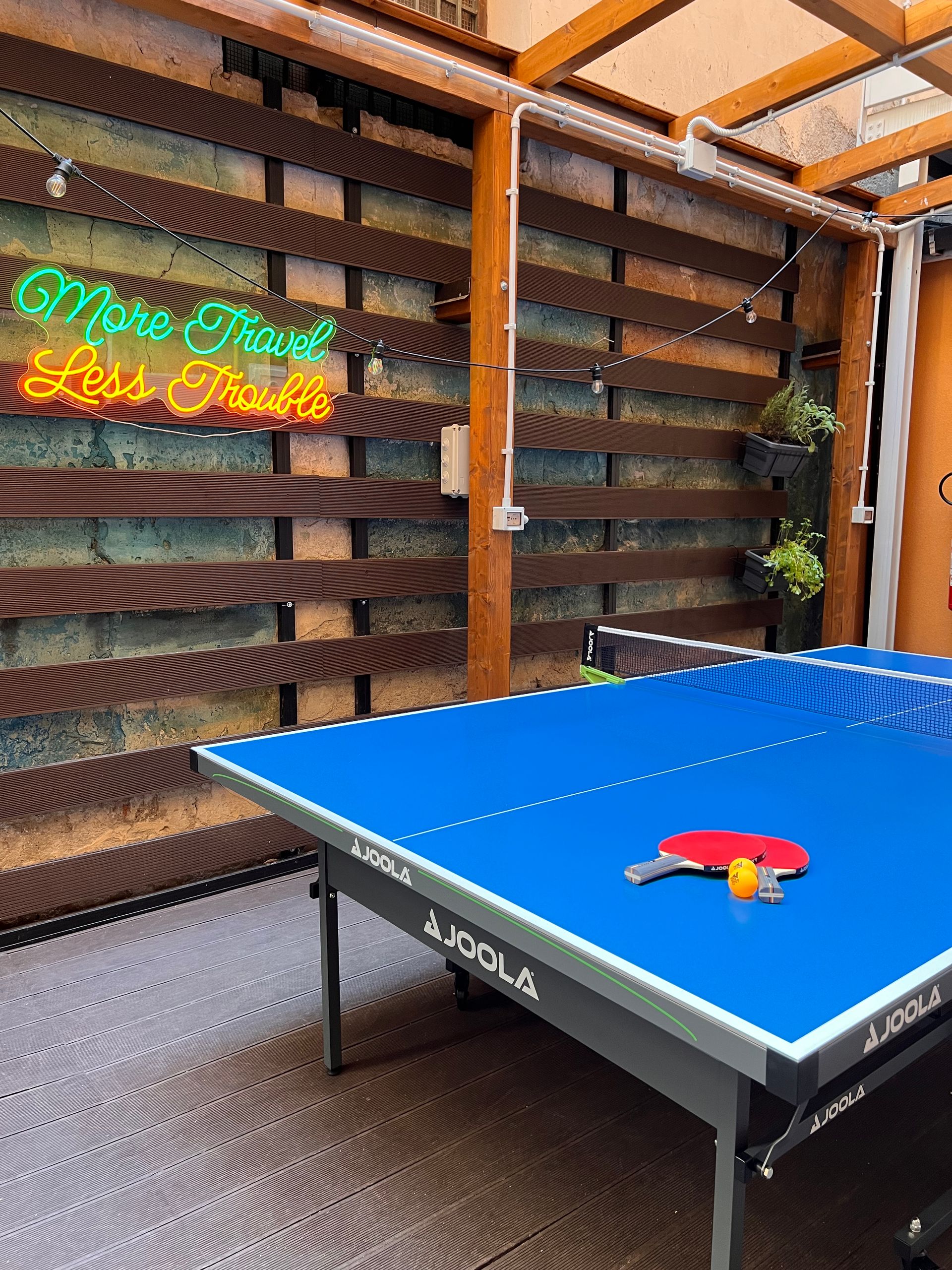 Tavolo da ping pong con racchetta e pallina, sotto un patio con un'insegna al neon che dice 