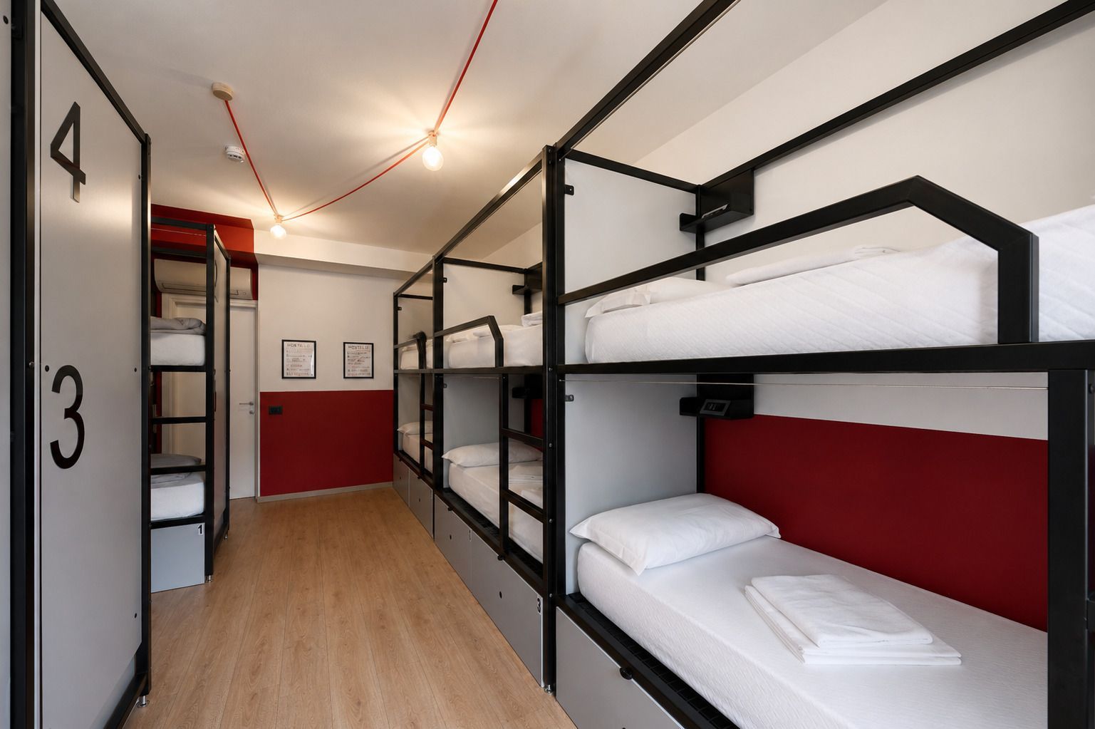 Dormitorio dell'ostello con più letti a castello, dettagli rossi e pavimento in legno.