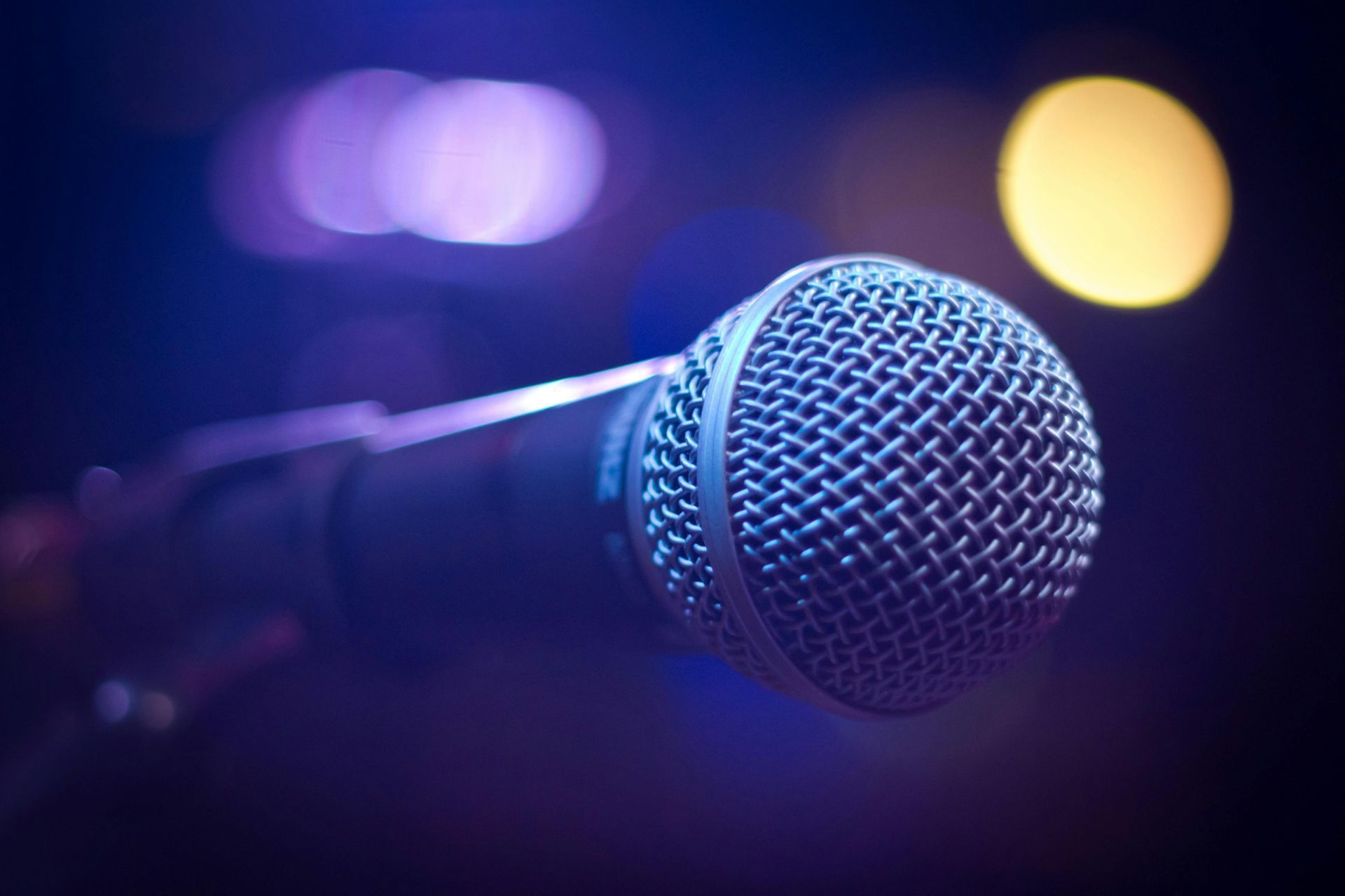 Primo piano di un microfono su un supporto con luci del palco viola e oro sfocate sullo sfondo.