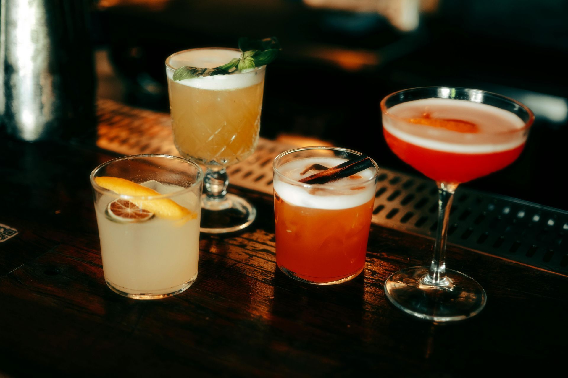 Foto di quattro cocktail colorati appoggiati su un bancone di un bar