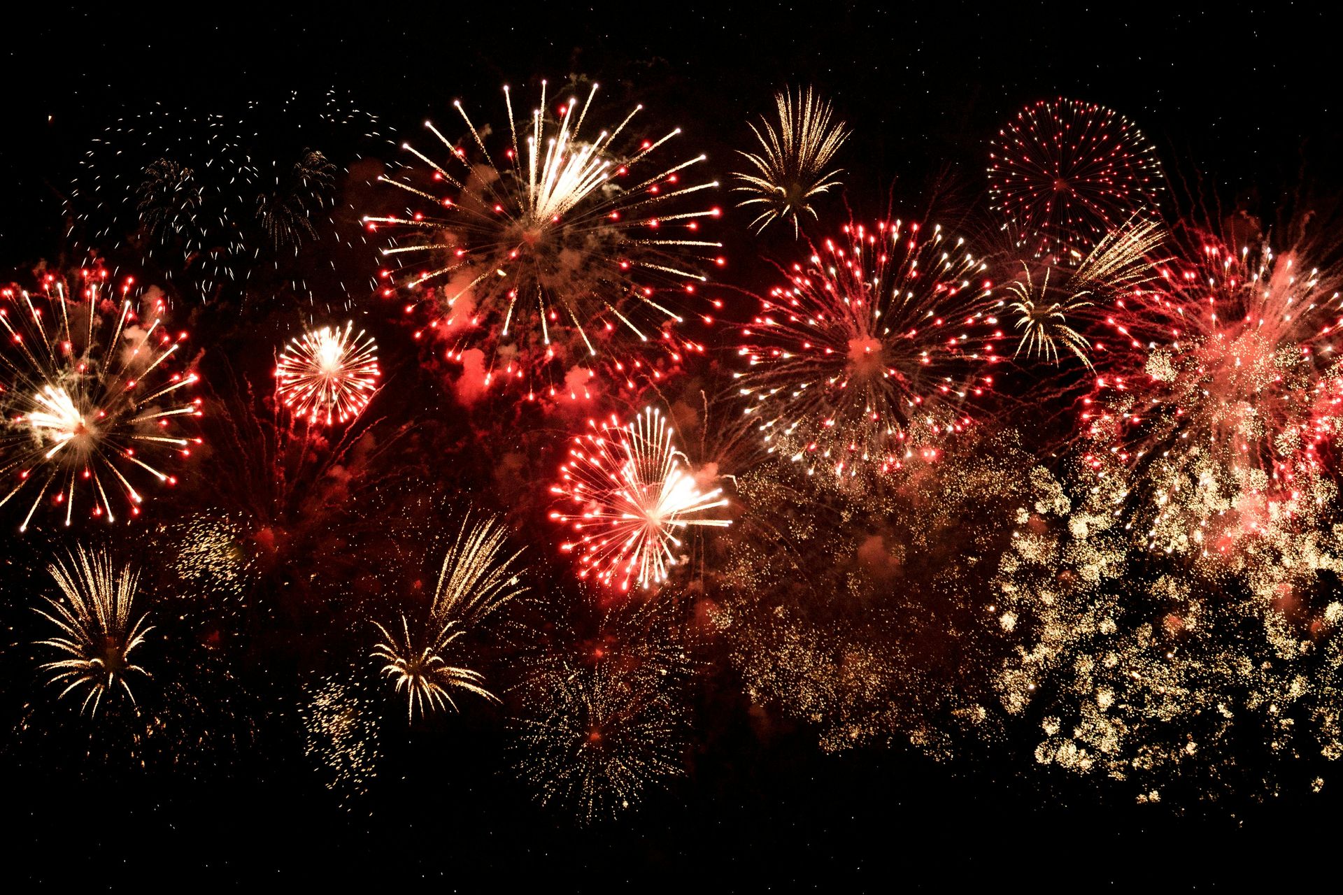 Fuochi d'artificio che esplodono in rosso, oro e bianco contro un cielo nero.