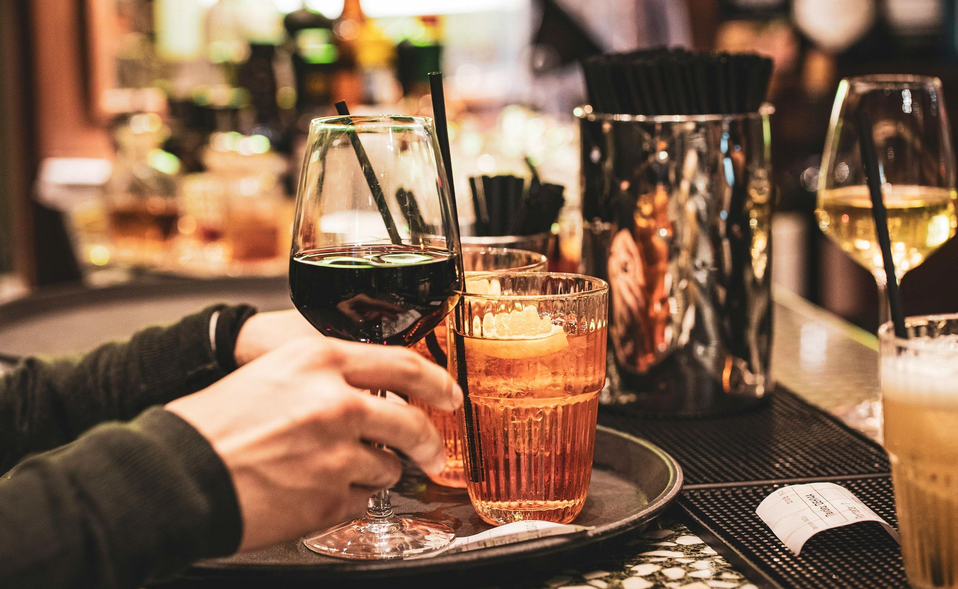 Persona che regge un vassoio con bevande al bar: vino rosso in un bicchiere, cocktail e caffè con schiuma.