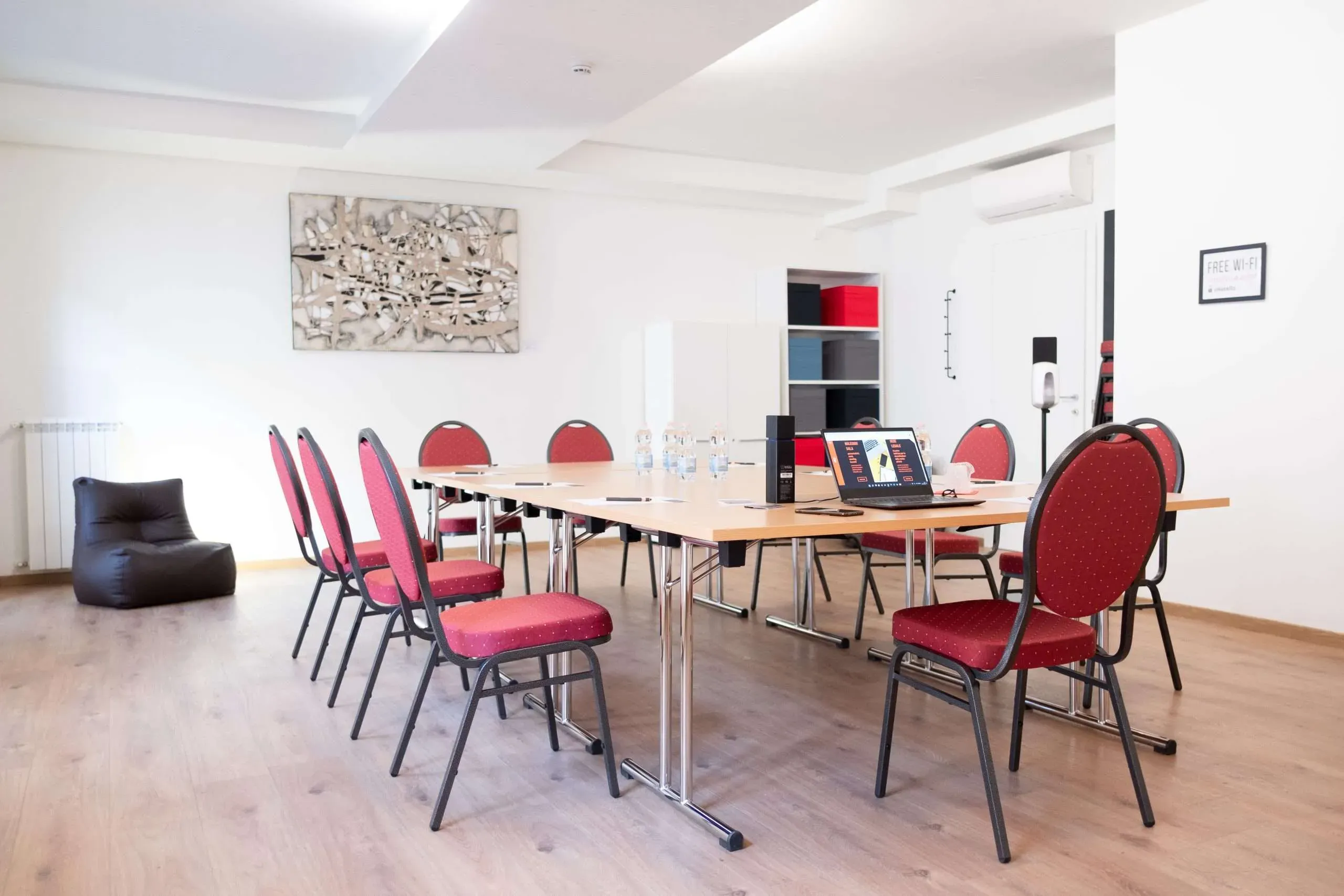 Sala conferenze con un lungo tavolo, sedie rosse e un computer portatile, il tutto in un ambiente molto luminoso.