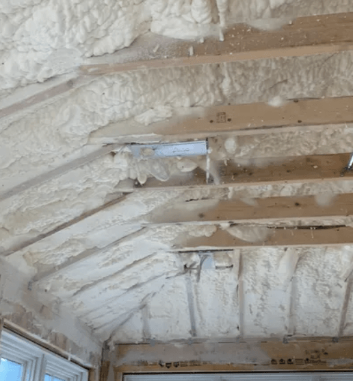 Foam insulation applied to the interior ceiling of a room, covering wooden beams and rafters.