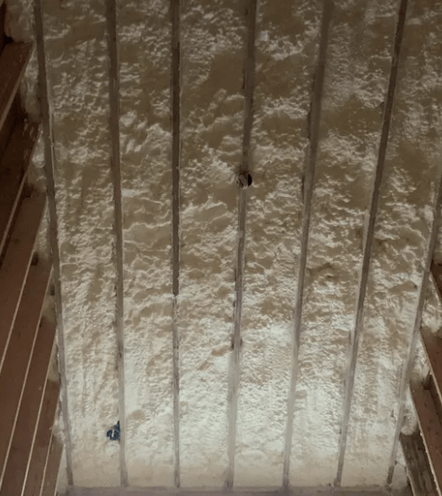 Attic ceiling with spray foam insulation between wooden rafters.