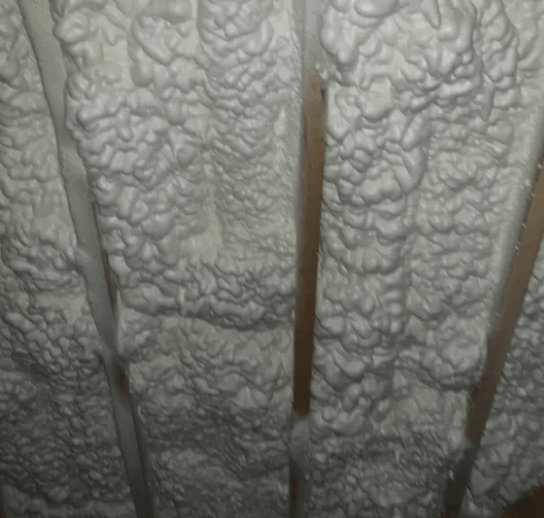White spray foam insulation fills the space between wooden rafters in an attic.