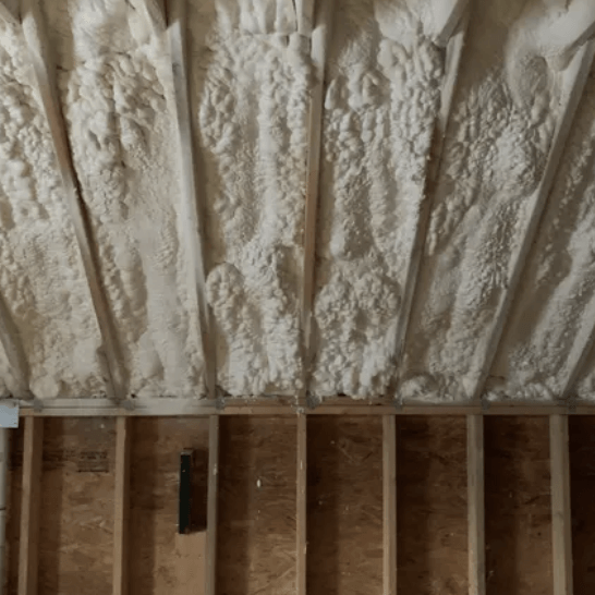 Spray foam insulation fills a wooden ceiling with exposed beams.