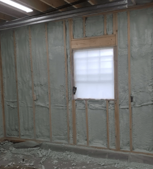 Wall construction with wooden studs and spray foam insulation around a window.