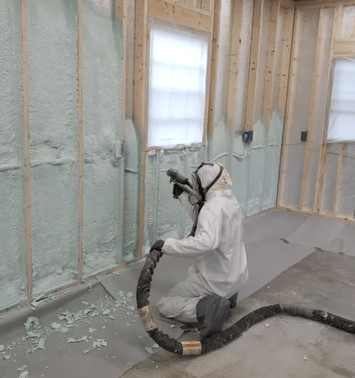 Person in protective suit spraying insulation foam on interior wall.