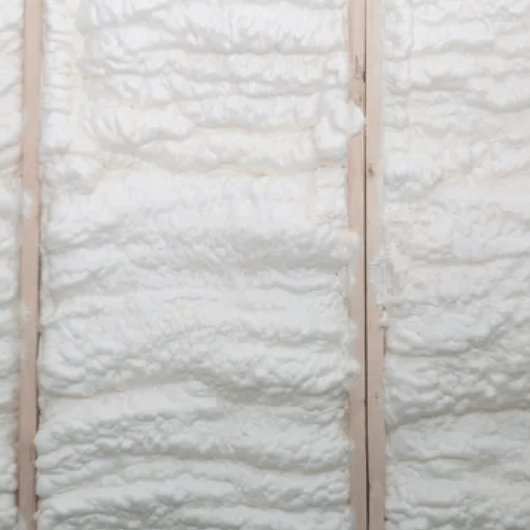 White spray foam insulation fills the space between wooden wall studs.