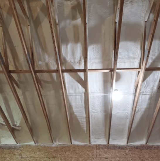 Interior view of an attic with spray foam insulation between wooden rafters.