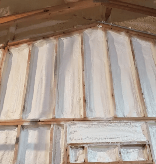 Interior wall with white spray foam insulation between wooden studs.