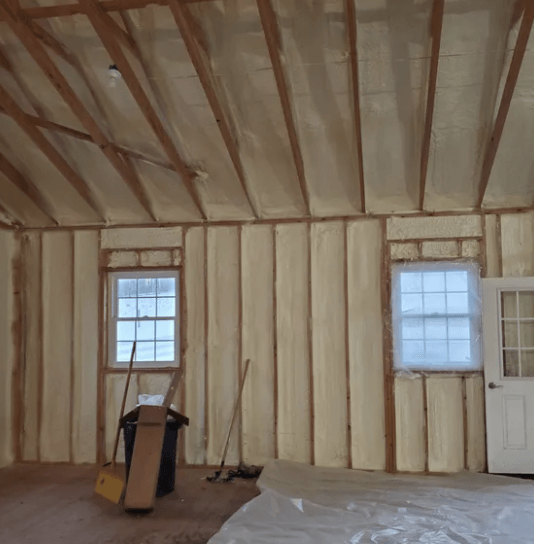 Interior of a building with spray foam insulation on walls and ceiling, including windows and a door.