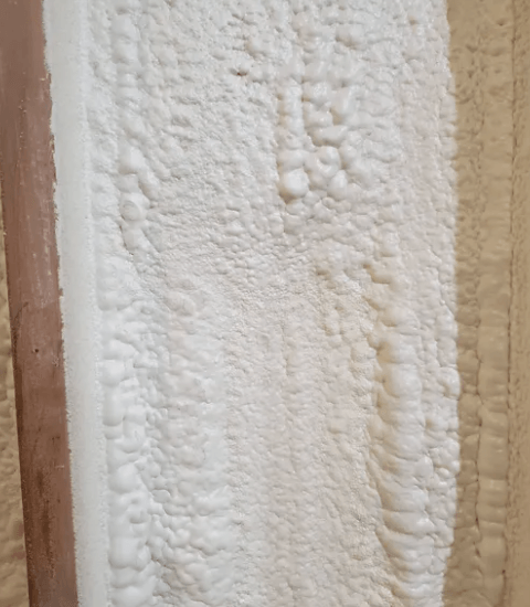 White spray foam insulation fills a wall cavity between wooden beams.