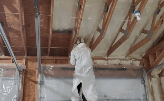 Person in protective suit spraying foam insulation in garage ceiling.
