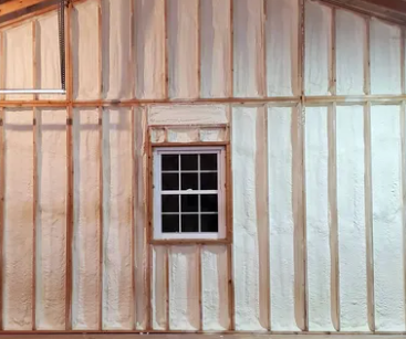 Interior wall with spray foam insulation between wooden studs, and a small window.