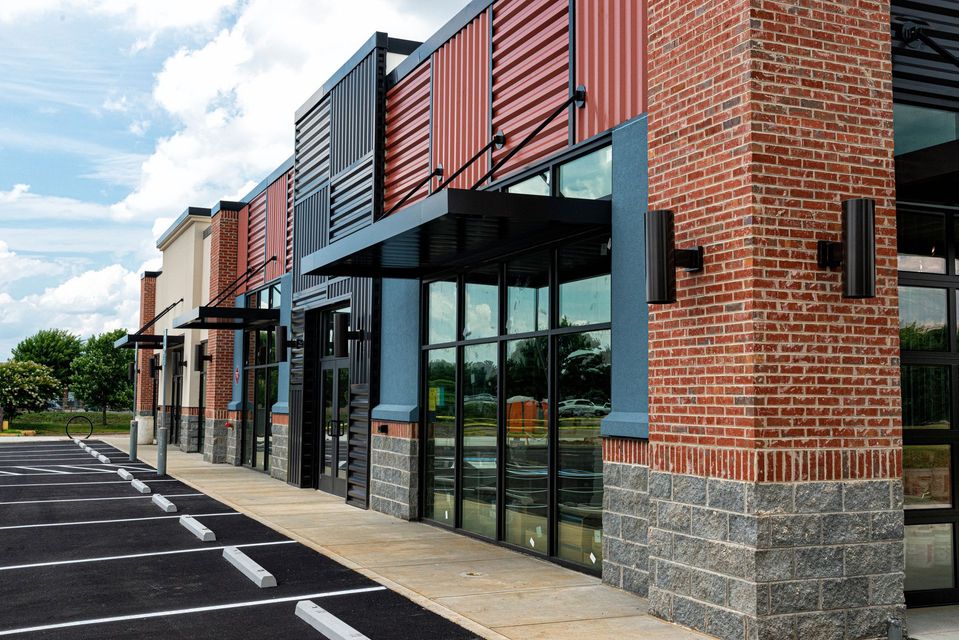 Modern brick-and-glass storefronts with red accents along a parking lot walkway
