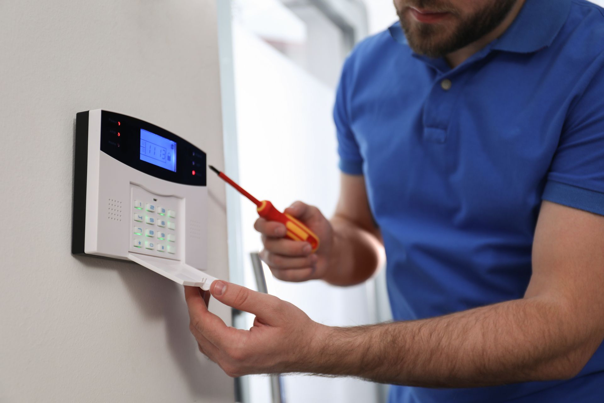 Technician using a screwdriver during alarm system installation on a wall keypad.