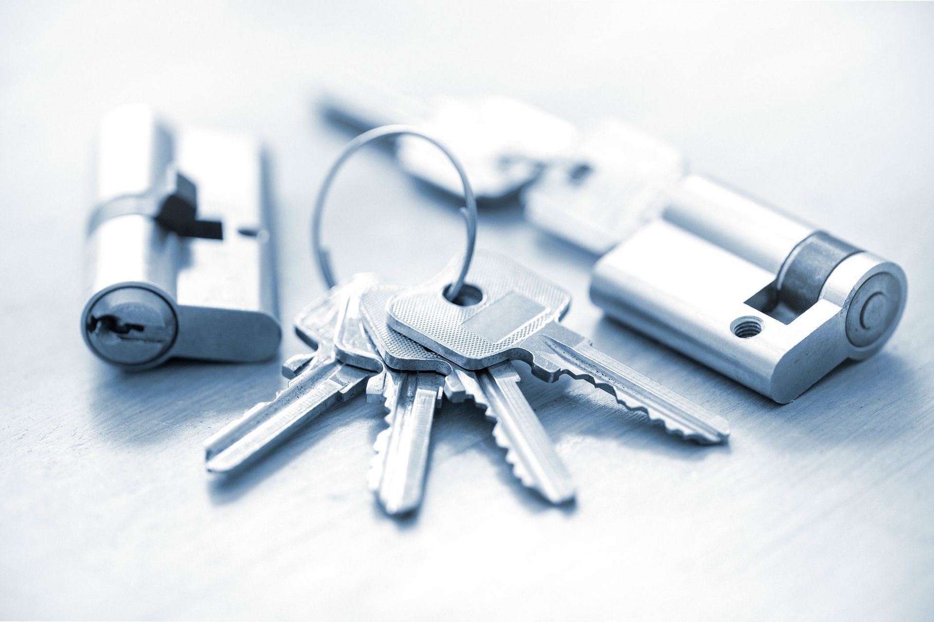 Silver keys on a keyring beside a lock cylinder and padlock on a white surface