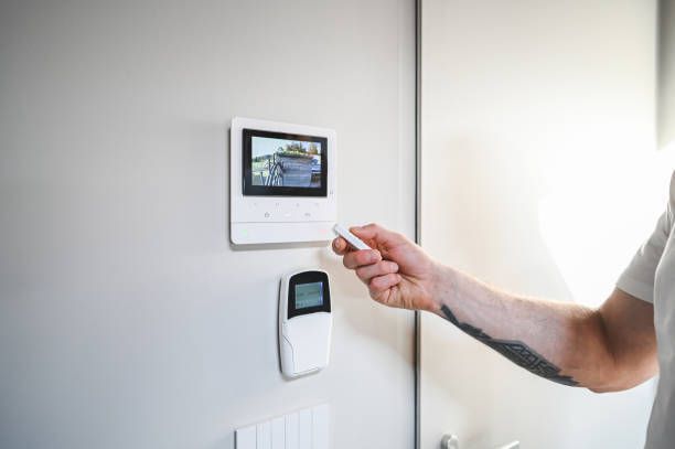 Hand reaching toward a wall-mounted smart thermostat in a bright room