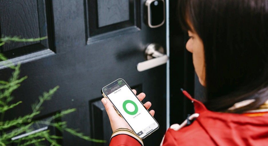 Person using a smartphone app near a black front door with a silver handle