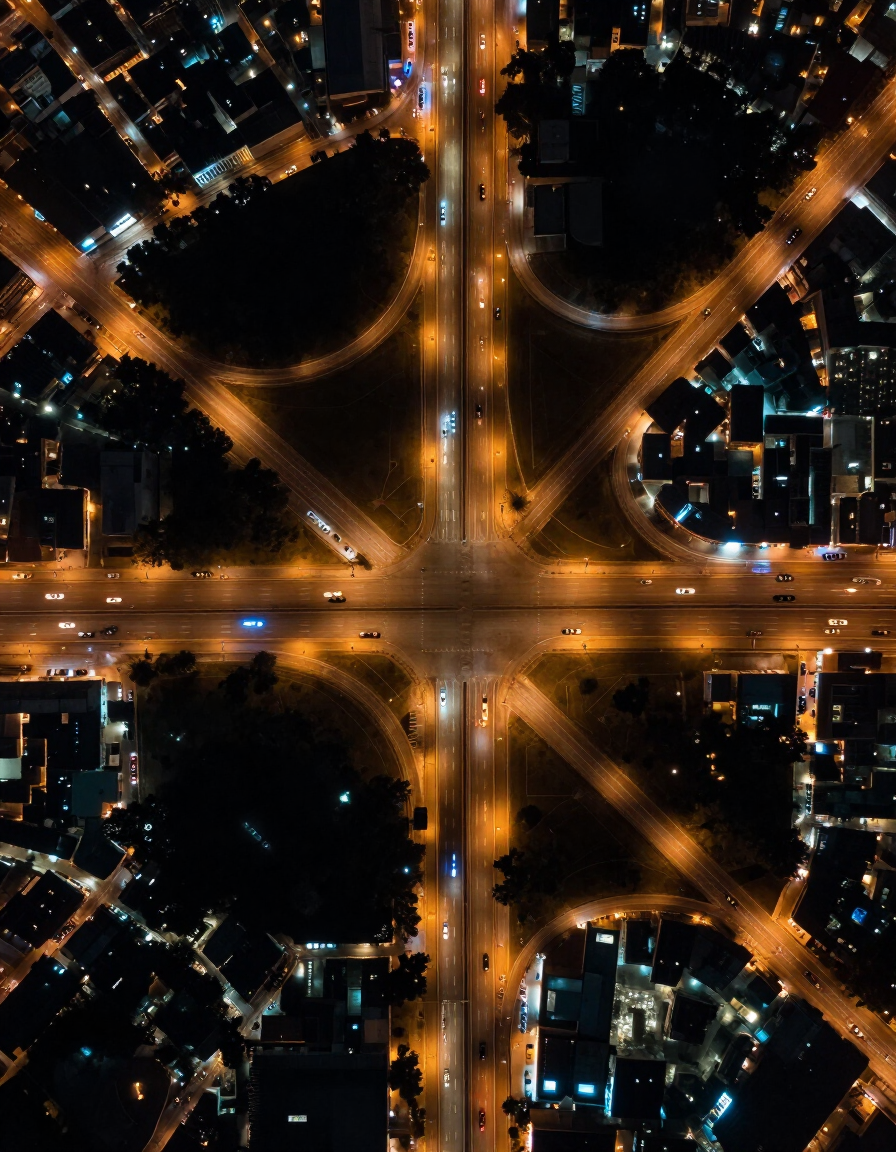 Vista aérea nocturna de una intersección iluminada de la ciudad con carreteras resplandecientes y edificios circundantes.