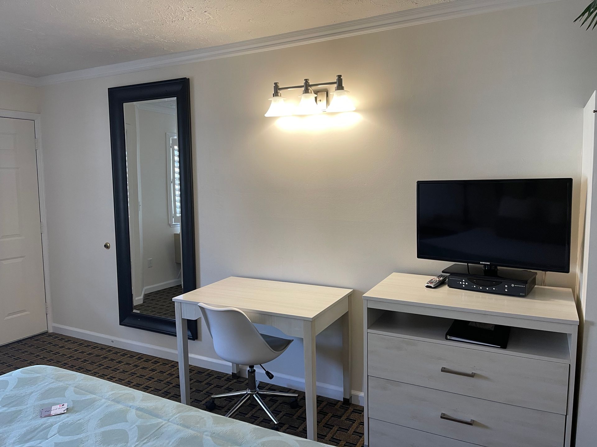 Bedroom with a large mirror, desk, dresser, TV, and overhead light.