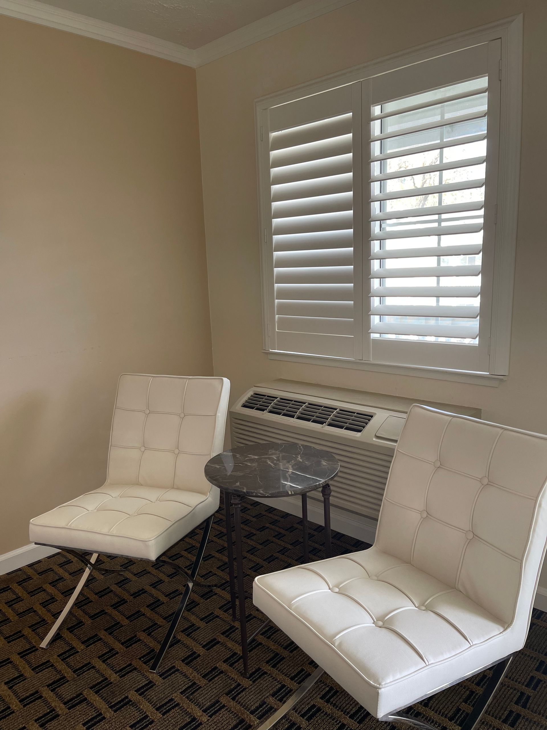 Two white chairs facing each other near a window with white shutters and an air conditioning unit.