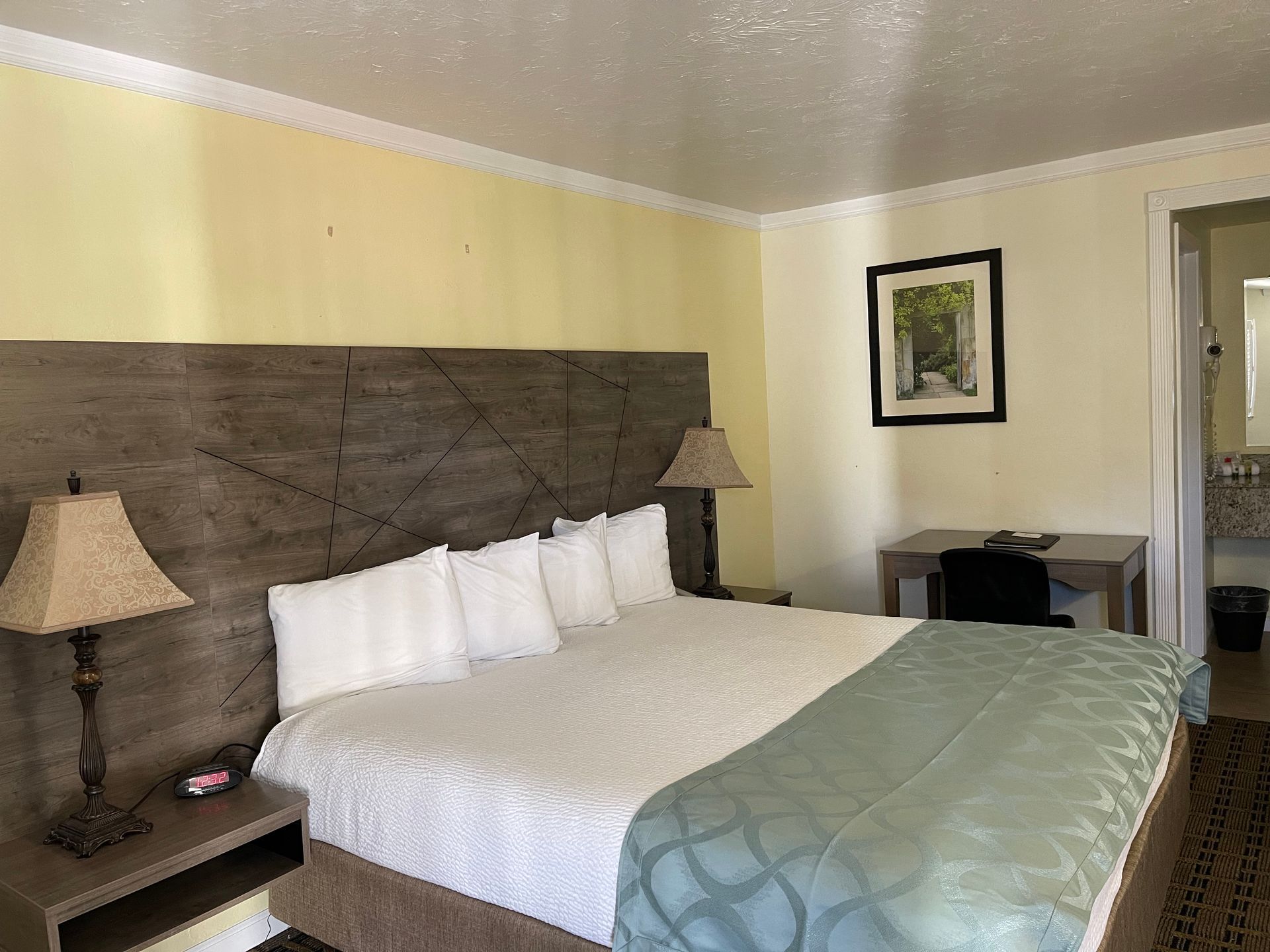 Bedroom with a king bed, nightstands, lamps, desk, and an open doorway to a bathroom. Yellow walls, wood headboard.